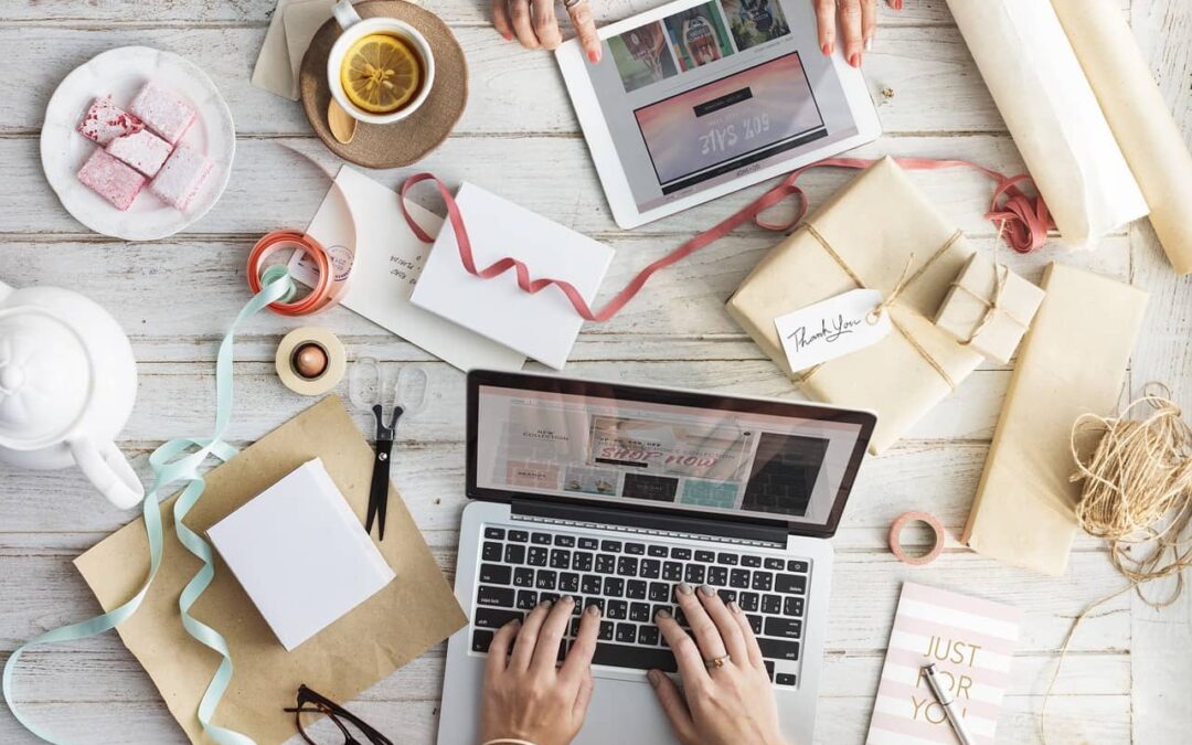 Arbeitsumgebung mit Laptop, Tablet, Geschenken und Dekorationsmaterialien. Zwei Personen arbeiten an digitalen und handgemachten Projekten